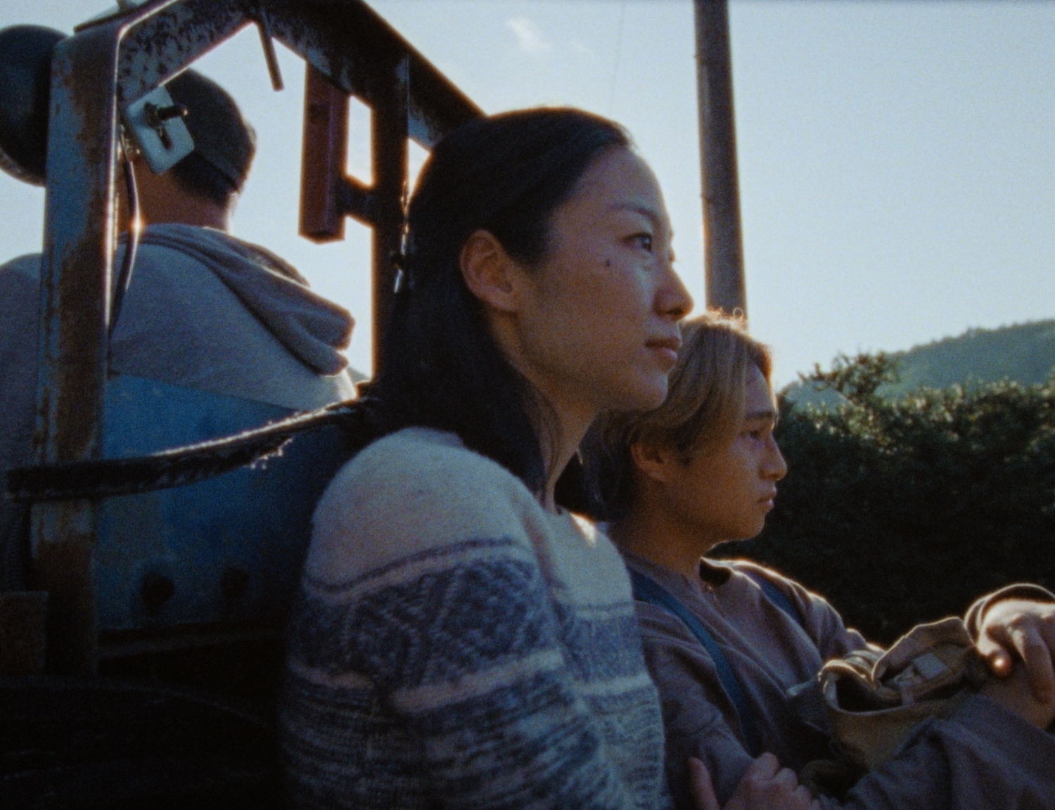 A mother and son sitting on the back of a small vehicle. Set in a mountainous region on a sunny day.