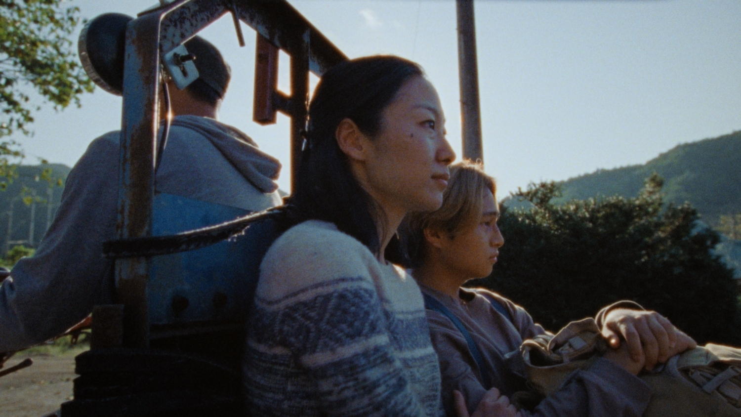 A mother and son sitting on the back of a small vehicle. Set in a mountainous region on a sunny day.