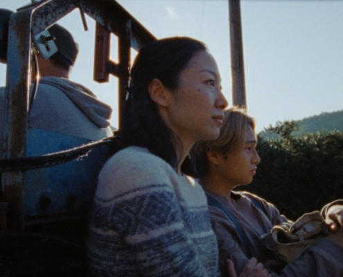 A mother and son sitting on the back of a small vehicle. Set in a mountainous region on a sunny day.