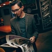 A person in a suit jacket stands in a room leafing through a magazine.