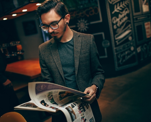 A person in a suit jacket stands in a room leafing through a magazine.