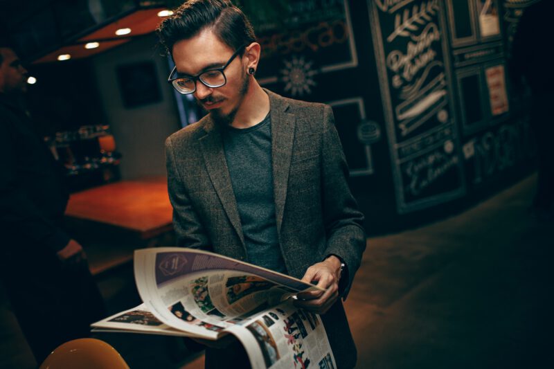 A person in a suit jacket stands in a room leafing through a magazine.
